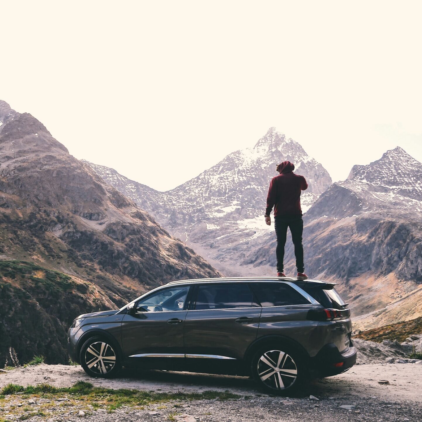A traveler standing on an SUV overlooking a mountain vista, embodying the freedom of a car rental deal from GlobalTravelGuideX.