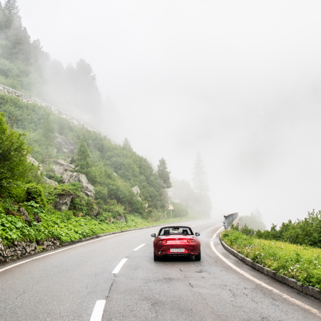 A red sports car on a misty mountain road, an example of the exciting luxury car rental options available on GlobalTravelGuideX.